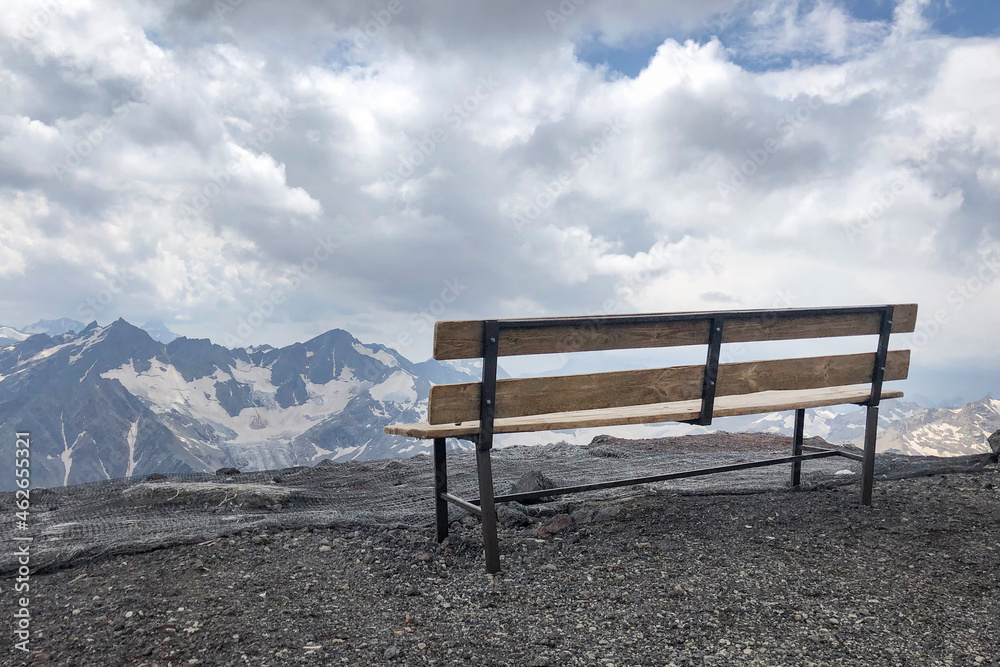 Old wooden bench on top of high winter mountain, cloudy sky on background, copyspace. Place for relaxation in mountains