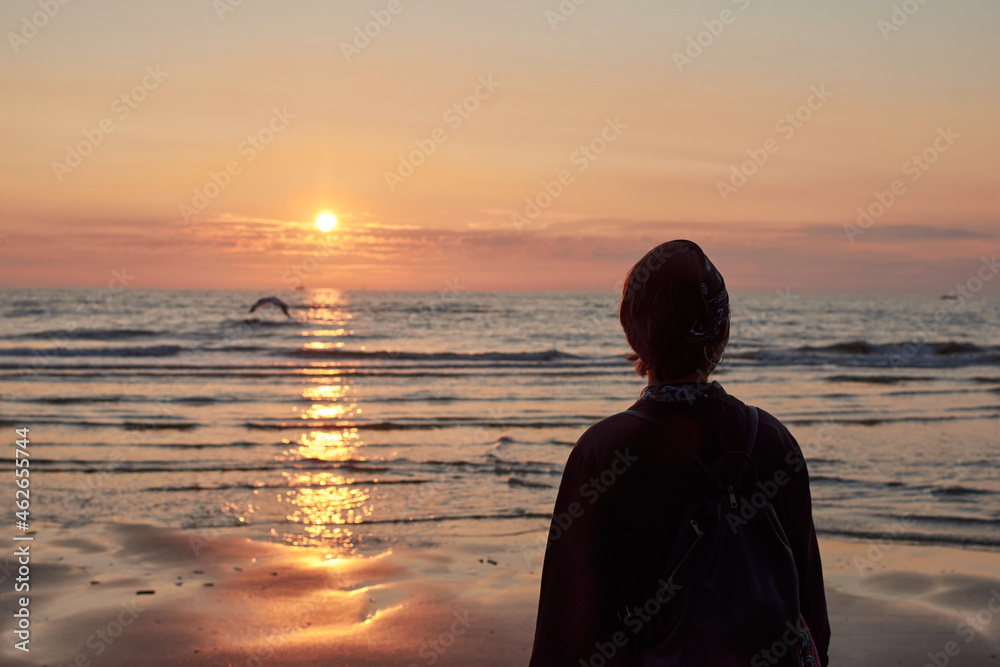 A silhouette of a woman standing on the beach during the sunset