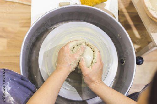 Female pottery artist hands shapes the clay on pottery wheel. Creative handmade craft.Top view. Ceramic art studio.