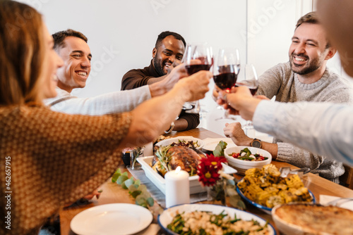 Multiracial happy friends drinking wine during thanksgiving dinner