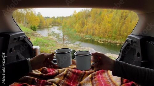 travel, tourism and camping concept - view to river from car trunk with couple under blanket toasting tea cups