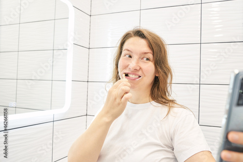 Young woman doing self portrait indoors. Home vacation portrait. Blogger selfie video. Alone in interior. Happy emotion. Smiling female person. Lifestyle action. Posing. Washing teeth