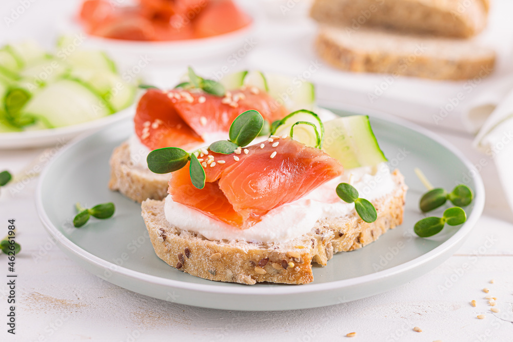 Toasts or open sandwiches with salted salmon, ricotta cream cheese, cucumber, sprouts and whole grain bread on white table. Healthy food, diet. Breakfast. Toasts or open sandwiches with salted salmon, ricotta cream cheese, cucumber, sprouts and whole grain bread on white table. Healthy food, diet. Breakfast.