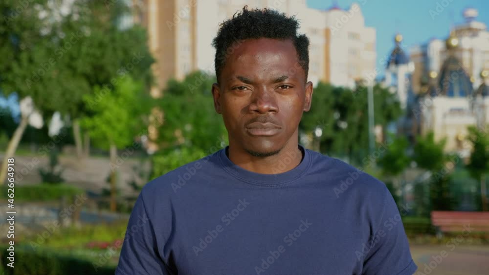 Close up Afro-American man student standing in park and looks camera. Portrait African adult male ethnic black freelancer wears blue t-shirt in summer Close up Afro-American man student standing in park and looks camera. Portrait African adult male ethnic black freelancer wears blue t-shirt in summer
