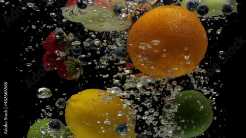 Slow motion mix strawberry, blueberry, lemon, lime, orange, half green and red apple falling into transparent water on black background. Fresh berry and fruits splashing in aquarium. Healthy food