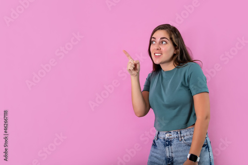 Young woman smiling with his finger pointing and looking at on light pink banner background with copy space.