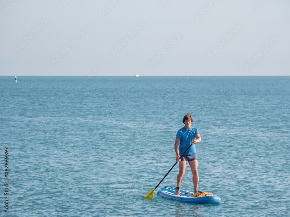Naklejka premium Paddle boarder. Sportsman paddling on stand up paddleboard. SUP surfing. Active lifestyle. Outdoor recreation. Vacation on seaside.