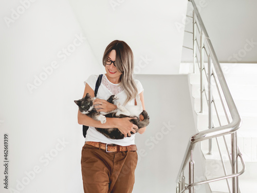 Smiling woman strokes stray cat on stairs. Volunteer is saving undomestic animal. White staircase in apartment building. Pet adoption. photo