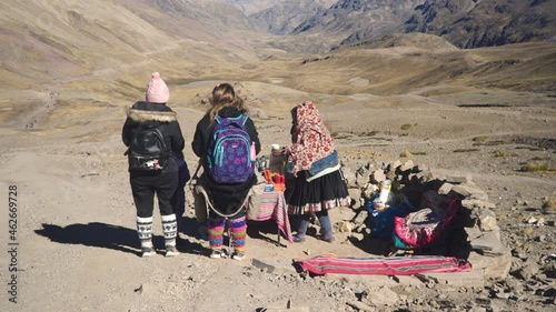 An elderly woman prepares coca tea for tourists on a rainbow mountain. View of the mountains and the valley.