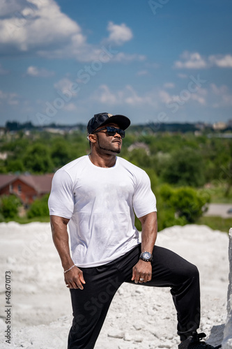Strong muscular man in whitr shirt on beautiful landscapes. Athlete on sunny day standing in nature. © Vadim