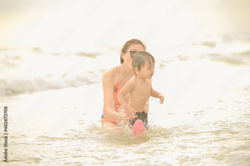 Happy family resting at beach in summer, Mother and baby boy feet at the sea foam at the sunlight water is moving Happy family resting at beach in summer, Mother and baby boy feet at the sea foam at the sunlight water is moving