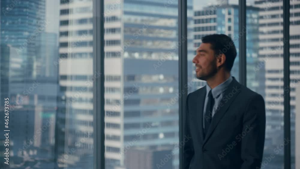 Thoughtful Young Businessman in a Perfect Tailored Suit Walking in His Modern Office Looking out of the Window on Big City with Skyscrapers. Successful Finance Manager Planning Project Strategy. Thoughtful Young Businessman in a Perfect Tailored Suit Walking in His Modern Office Looking out of the Window on Big City with Skyscrapers. Successful Finance Manager Planning Project Strategy.