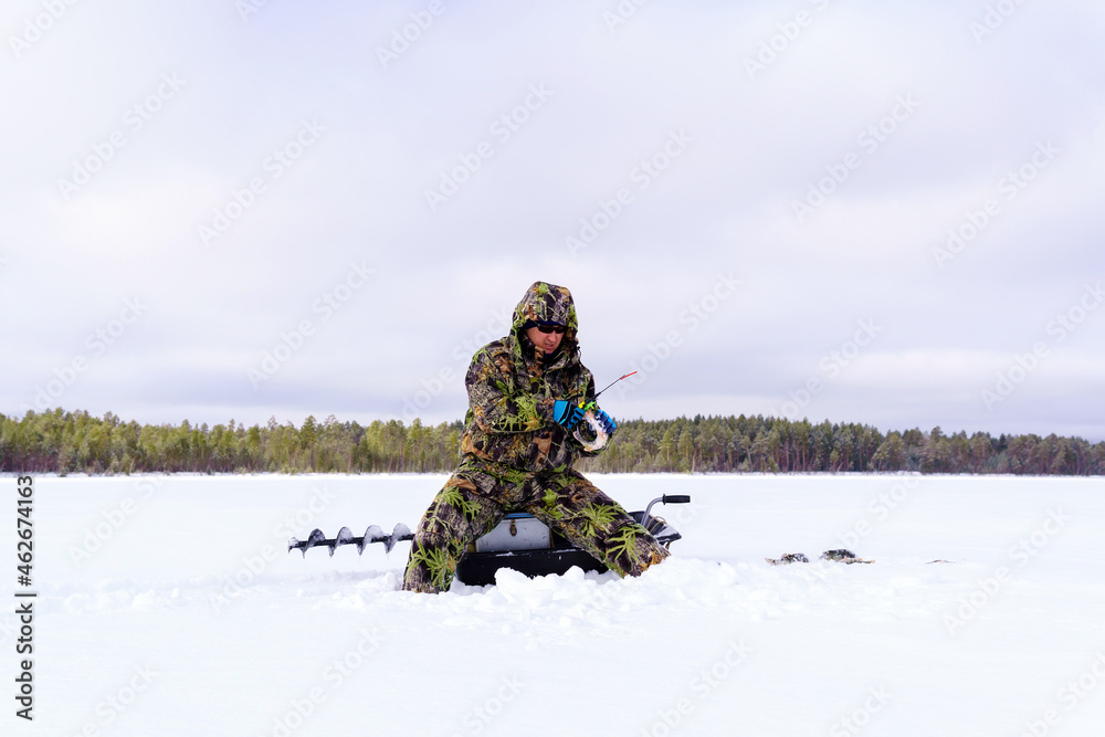 A fisherman in special clothes catches fish in winter on the lake. The concept of survival in the wild in winter