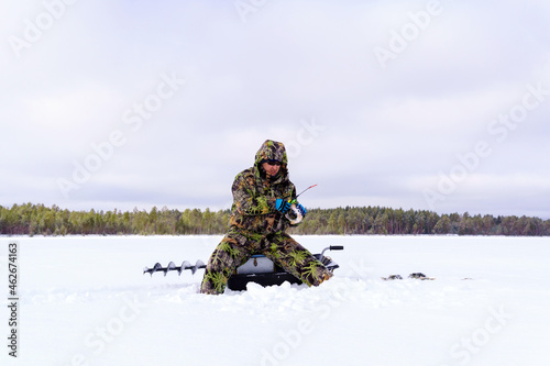 A fisherman in special clothes catches fish in winter on the lake. The concept of survival in the wild in winter