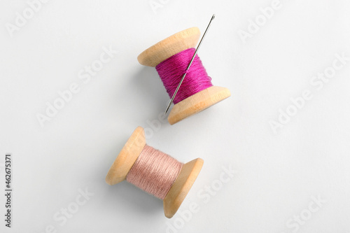Colorful sewing threads with needle on white background, top view