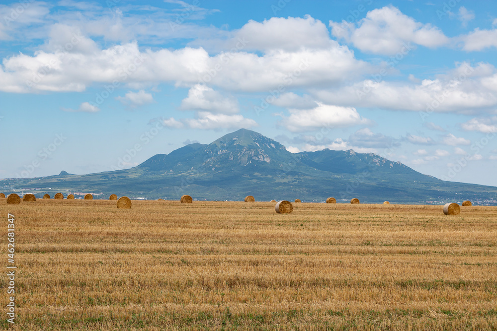 The region of the Caucasian Mineral Waters. Harvest time: a large round bale of hay on a mown summer meadow, photographed in close-up, with mountains surrounding fields in the background. The region of the Caucasian Mineral Waters. Harvest time: a large round bale of hay on a mown summer meadow, photographed in close-up, with mountains surrounding fields in the background.
