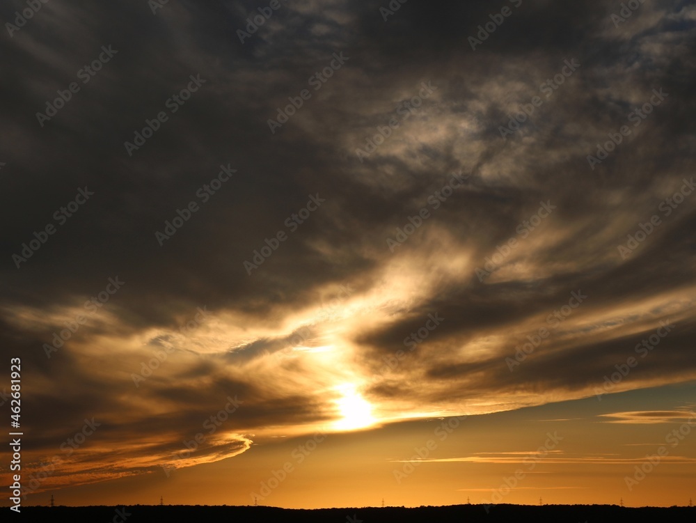 golden hour in cloudy space, stormy gray clouds illuminated by the golden setting sun, beautiful evening stormy sky, weather phenomena in the sky at sunset time
