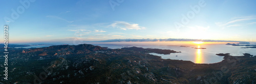 View from above, aerial shot, stunning panoramic view of a green coastline bathed by a calm water during a beautiful sunrise. Costa Smeralda, Sardinia, Italy.