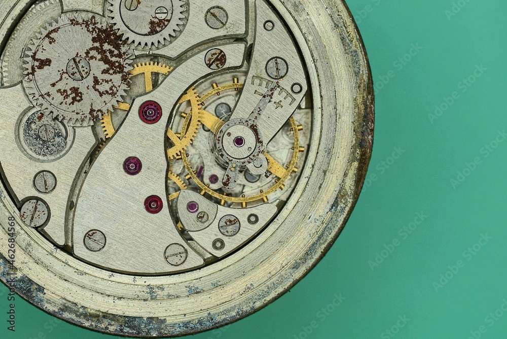 metal mechanism of an old gray round clock lies on a green table