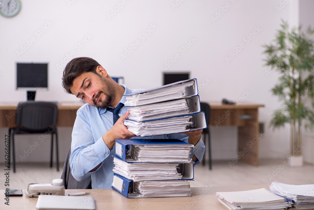Young male employee and too much work in the office Young male employee and too much work in the office