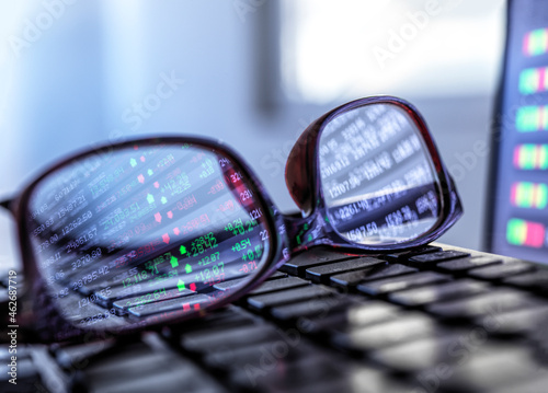 Stock market data reflecting in eyeglasses lying on laptop keyboard