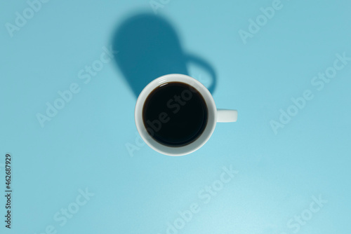 White cup with coffee on a blue background. Minimalism, shadow in the form of a bullhorn