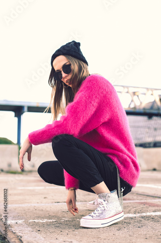 Portrait of fashionable young woman wearing sunglasses, cap and pink knit pullover