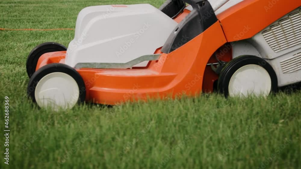 Close up tracking shot of a mowing the grass in the backyard with an electric lawn mower. Slow motion Close up tracking shot of a mowing the grass in the backyard with an electric lawn mower. Slow motion