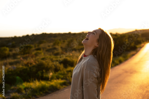 Laughing young woman on country road at sunset