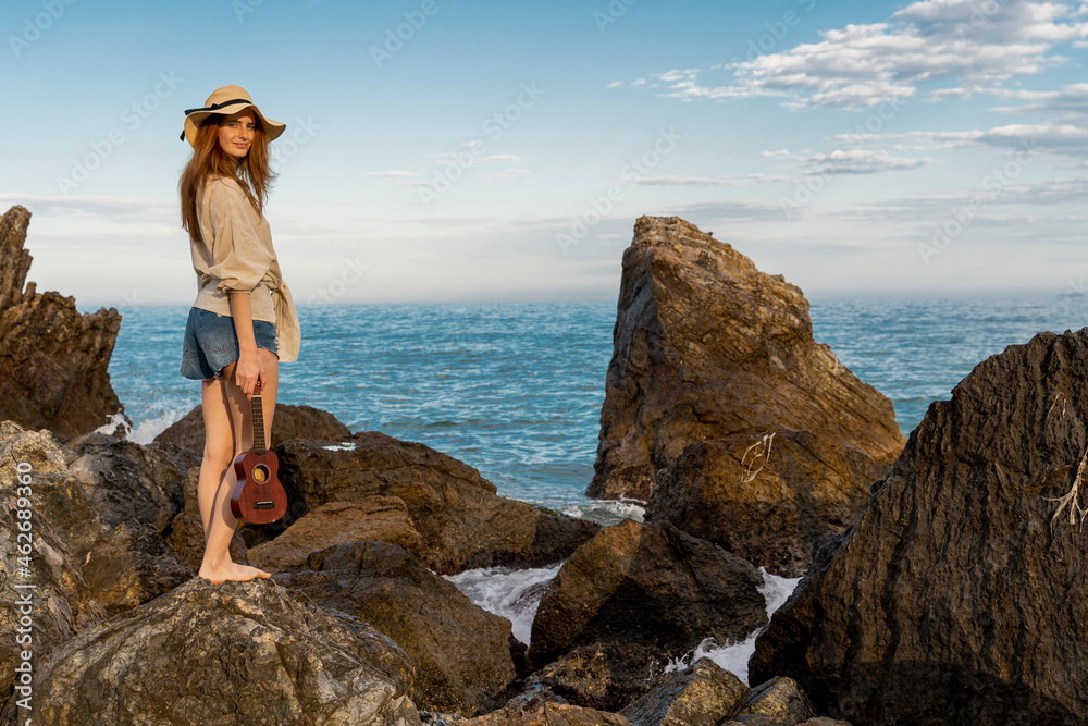 Smiling redheaded young woman with ukulele standing on rock Smiling redheaded young woman with ukulele standing on rock