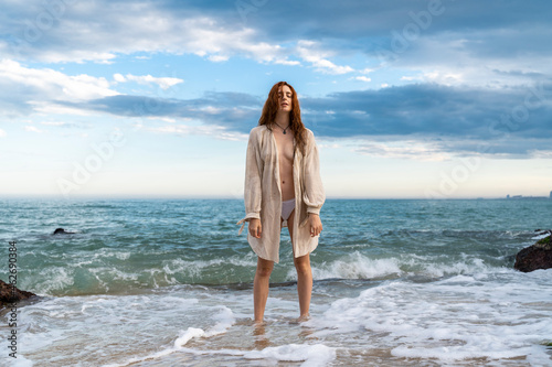 Redheaded young woman standing in front of the sea photo