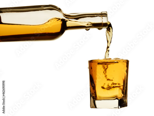 Whiskey from the bottle is poured into a glass with bubbles and drops. Isolated on a white background