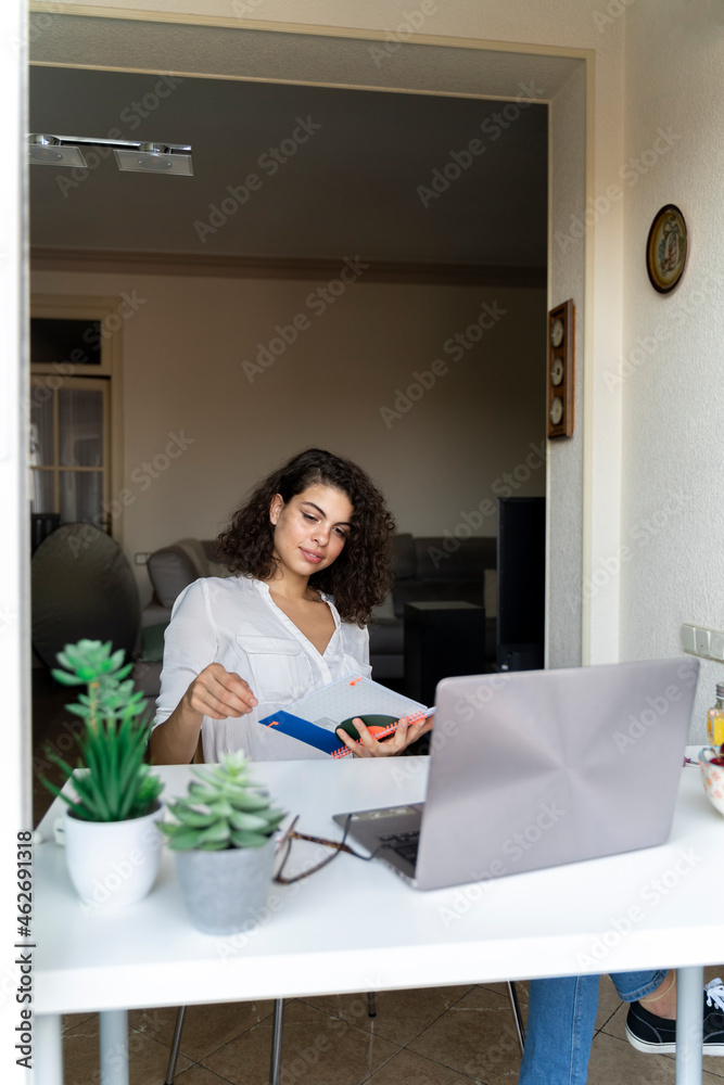 Young woman with notepad and laptop at desk at home Young woman with notepad and laptop at desk at home