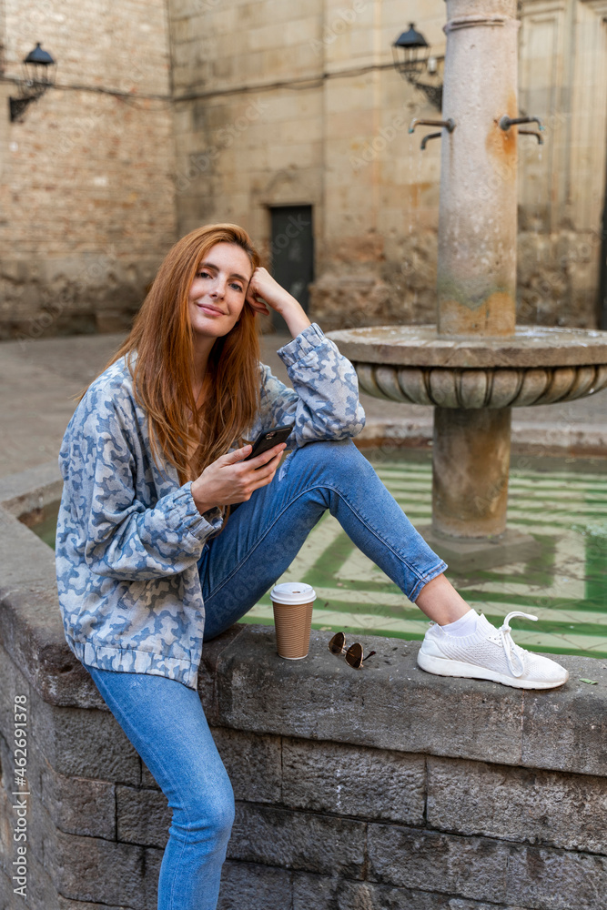 Woman using smartphone sitting on a fountain Woman using smartphone sitting on a fountain
