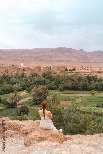 Back view of young womansitting on a rock looking at the city, Ouarzazate, Morocco photo