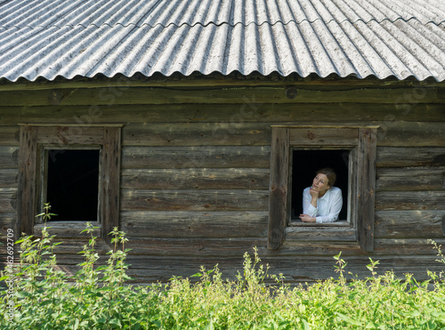 Woman looking out of window of an old wooden village house
