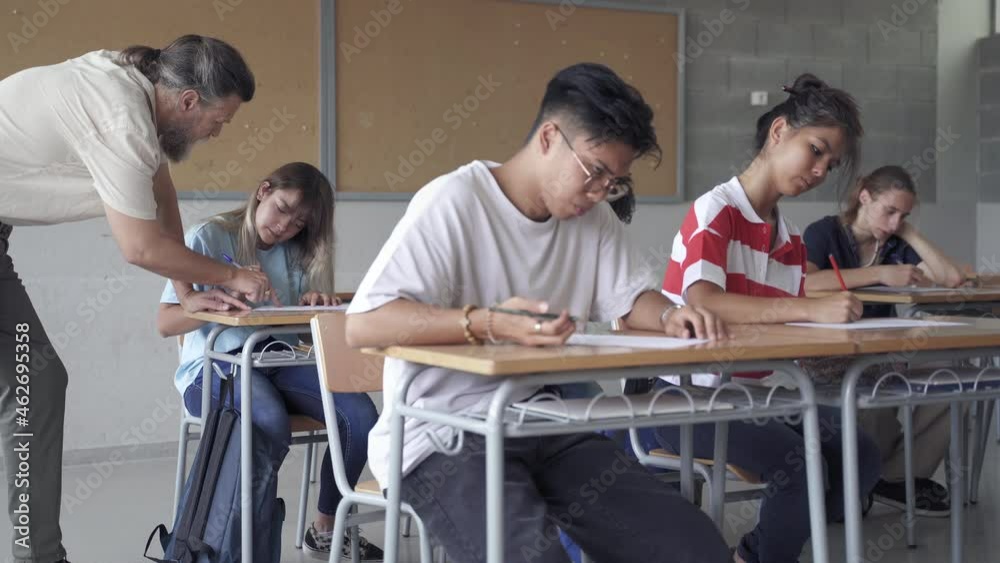 Asian student taking exam and professor explaining exercise to teenager pupil in secondary school classroom Asian student taking exam and professor explaining exercise to teenager pupil in secondary school classroom