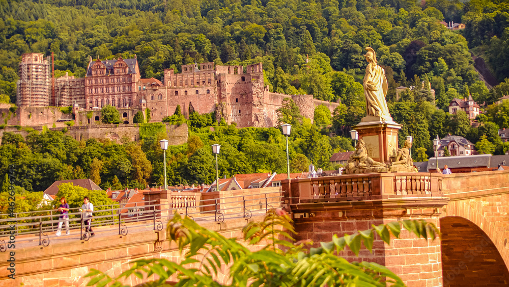 Old statue of Minerva at city bridge and castle as fortress in background in Heidelberg historical downtown, Germany, cityscape, sunny summer day.