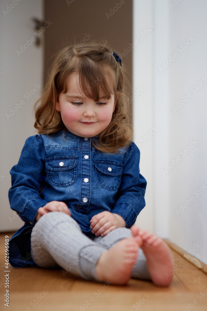 Portrait of smiling toddler girl sitting on the floor at home watching her bare feet Portrait of smiling toddler girl sitting on the floor at home watching her bare feet