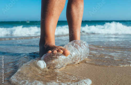 Foot of man stepping on empty plastic bottle lying on the beach, close-up