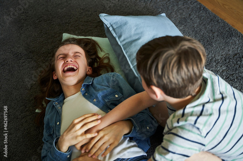 Boy tickling his older sister lying on carpet at home