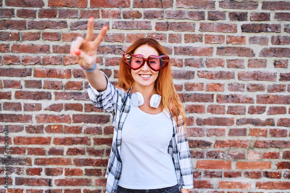 Gorgeous young woman in heart-shaped glasses smiling at camera and making peace gesture Gorgeous young woman in heart-shaped glasses smiling at camera and making peace gesture