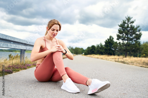 Woman sitting on ground and holding knee after injury during workout photo