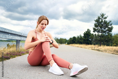 Woman sitting on ground and holding knee after injury during workout