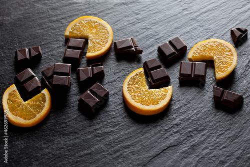 Cocolate pieces with orange slices on black slate