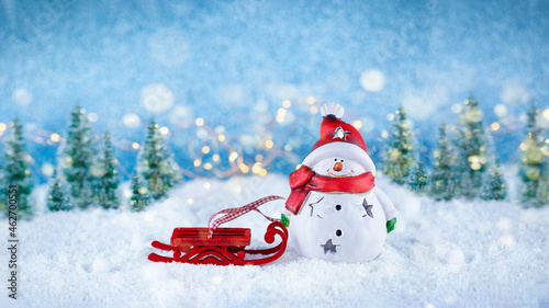 Happy snowman with red sleigh on snow. Christmas background with glitter bokeh