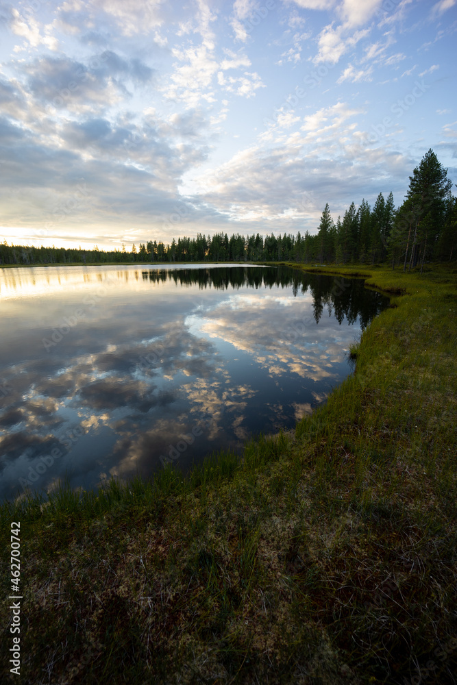 An epic lake view in Sweden near Glommersträsk. with open and cloudy sky and reflecting lake surface and a setting sun.