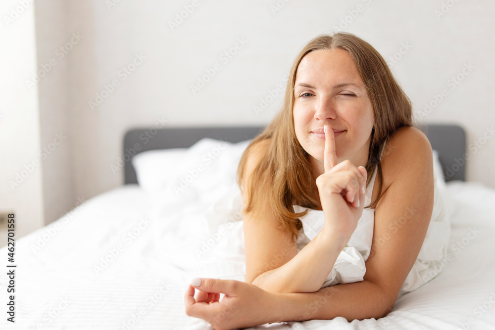 Young smiling attractive brunette woman lies in a big white bed