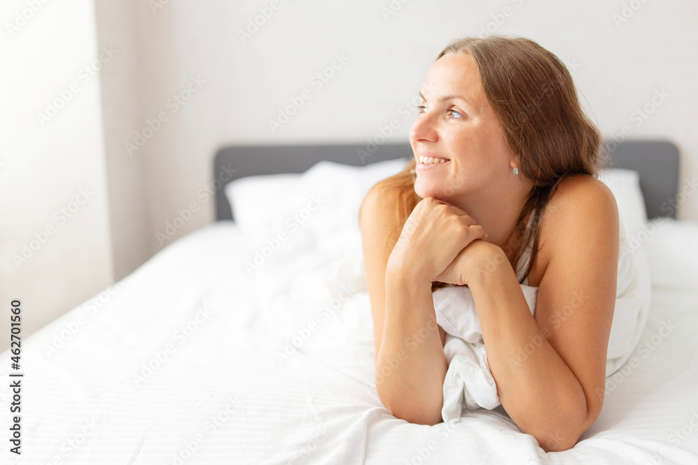 Young smiling attractive brunette woman lies in a big white bed Young smiling attractive brunette woman lies in a big white bed