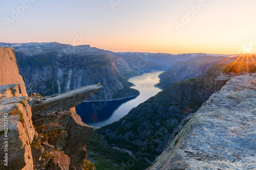 A man sits on the mountain's cliff edge of Trolltunga throning over Ringedalsvatnet watching the sunset in the snowy Norwegian mountains near Odda, Rogaland, Norway. photo